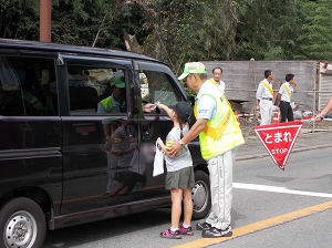 児童が交通安全ポスターの入ったティッシュを運転手に手渡す様子の写真